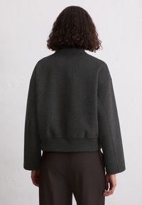 Donkergrijze, geknipte wollen jas met een hoge hals, geribbelde boord en brede mouwen, met een gladde textuur en een minimalistisch ontwerp.