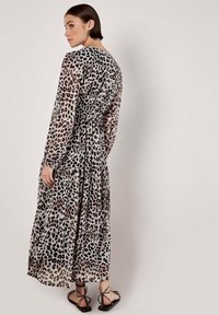 Langes, durchscheinendes Kleid mit Leopardenmuster, ausgestattet mit langen Ärmeln, einer taillierten Taille und einem mehrlagigen Rock, kombiniert mit flachen Sandalen.