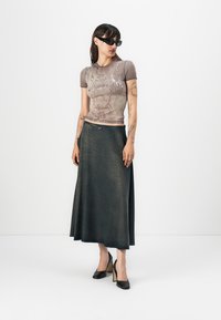 Grå grafisk t-skjorte med korte ermer, kombinert med en lang, mørk denimskjørt. Svart høyehælede sko fullfører antrekket.
