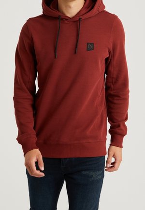 Sweatshirt à capuche rouge en tissu texturé avec un patch logo à l'avant, doté de cordons noirs et de poignets et d'un ourlet côtelés.