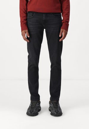 Black denim jeans with a slim fit, five pockets, and subtle stitching. Paired with black athletic shoes and a red sweater.