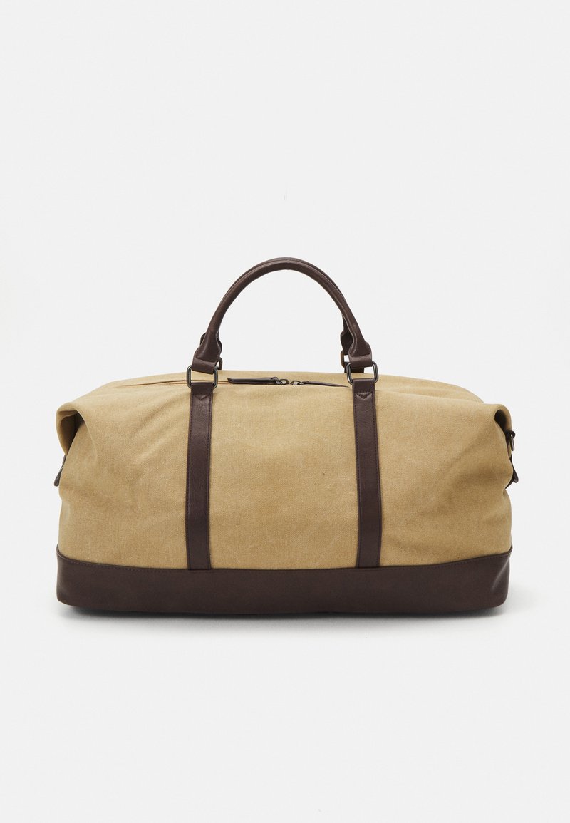 Beige canvas duffel bag with dark brown leather accents, dual handles, and zipper closure. Rectangular shape with soft sides.