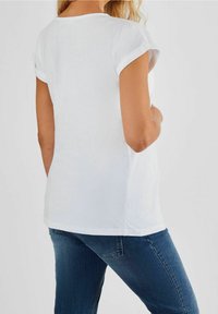 Biała koszulka z krótkim rękawem, z podwiniętymi mankietami, wykonana z miękkiej bawełny, okrągły dekolt i luźny krój, w zestawieniu z ciemnoniebieskimi dżinsami.