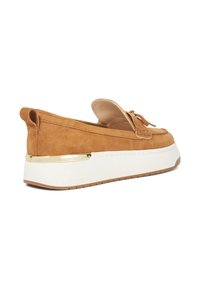 Tan suède instap schoenen met een witte chunky zool, voorzien van een gouden accent op de hak en een decoratieve strik aan de voorkant.
