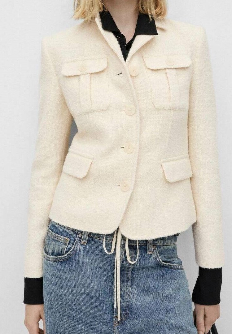 Cremefarbener Blazer aus Wollmischung mit strukturiertem Design, zwei Brusttaschen und einreihiger Knopfleiste, kombiniert mit Jeans.