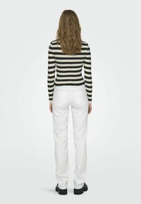 Top a maniche lunghe a righe nero e crema con design aderente, abbinato a jeans bianchi a gamba dritta e scarpe chunky nere.