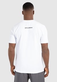 Hvid bomulds T-shirt med korte ærmer og rund hals, med "SMILODOX" trykt i sort på den øverste del af ryggen.
