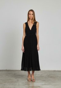 Schwarzes ärmelloses Kleid mit V-Ausschnitt, figurbetontem Oberteil und fließendem Rock. Weicher Stoff, Midi-Länge und subtiler Faltenwurf.