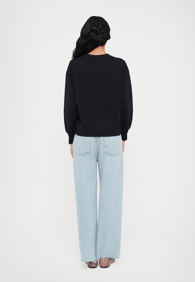 Navy sweater with a relaxed fit, paired with light blue wide-leg jeans. Distressed hem on jeans, with two back pockets visible.