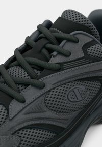 Pantofii sport gri au un design care îmbină texturi din plasă și suede, cu o formă rotundă, șireturi întunecate și un logo pe lateral, evidențiat prin accente contrastante.