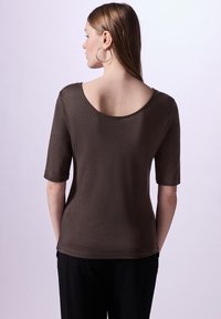 Top de punto marrón con escote redondeado y mangas cortas. Textura suave, forma ajustada y diseño de longitud media. Combinado con pantalones negros.