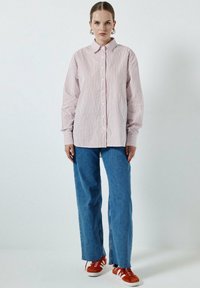Camicia a righe bianca e rossa, abbinata a jeans blu a gamba dritta e sneakers arancioni, con una vestibilità rilassata e maniche lunghe.