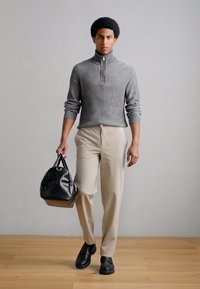 Maglione grigio a coste con zip, pantaloni beige su misura, borsa nera con texture e scarpe scure. Design minimalista con palette di colori neutri.