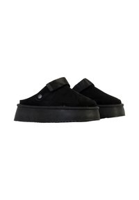 Chaussures plates à enfiler noires avec des brides larges ajustables et des détails de boutons, présentées côte à côte sur un fond blanc.