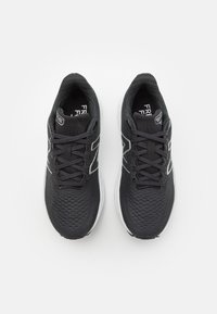 Černé atletické boty s texturovaným síťovaným svrškem, kontrastní bílou podrážkou a reflexními prvky. Mají tradiční zavazování na tkaničky.