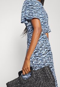 Blå mönstrad klänning med korta ärmar, texturerad tyg, insydd midja och en svart vävd handväska med ett stabilt handtag.