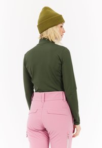 Olijfgroene lange mouwen top met een hoge kraag, gecombineerd met roze broek met een riem en zakken. Wol gebreide beanie in olijfgroen.