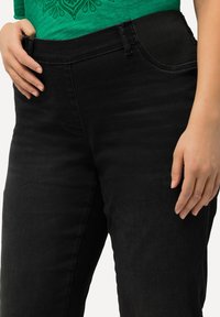 Jeans negros de cintura alta con un acabado suave, cinturilla elástica y un sutil detalle en los bolsillos, diseñados para la comodidad y el ajuste.