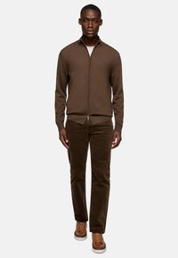 Brown zip-up sweater with ribbed texture, paired with dark brown corduroy pants and brown sneakers. Simple design, fitted silhouette.