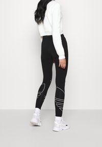 Svarta tights med vita linjemönster, hög midja och smal passform, kombinerat med en kort vit tröja och vita träningsskor.