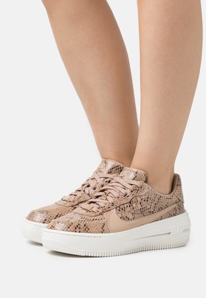 Zapatillas marrón claro con un patrón de piel de serpiente, diseño con cordones y suela de goma blanca con acentos texturizados y logotipo de la marca.