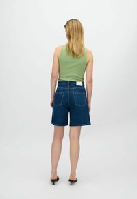 Débardeur vert côtelé associé à un short en denim bleu foncé, avec taille haute et ourlet effiloché. Poches arrière classiques visibles.