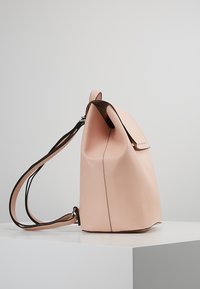 Posliinin vaaleanpunainen nahkainen reppu, jossa on minimalistinen muotoilu, taitettu yläosa, säädettävä olkahihna ja sileä pinta.