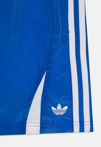Shorts de sport bleus en tissu léger avec une texture en grille. Présentent trois bandes blanches sur le côté et un logo brodé.