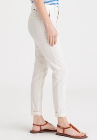 Krämfärgade slim-fit byxor med uppvikta fållar, två bakfickor och en slät textur, kombinerat med bruna platta sandaletter.