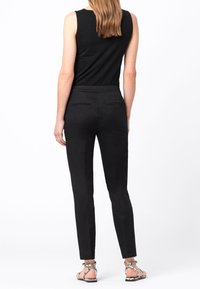 Pantalons noirs ajustés avec une texture lisse, longueur cheville, dotés de deux poches arrière et d'une taille plate. Associés à des sandales à brides.