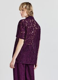 Camicetta viola in pizzo con maniche corte, caratterizzata da motivi floreali e una vestibilità ampia, abbinata a pantaloni coordinati, mostrando una trama intricata.