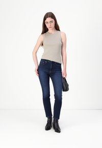 Světle béžový top bez rukávů, tmavě modré skinny džíny, černé kotníkové boty a malá černá taška. Hladká látka, přiléhavý střih a minimální detaily.