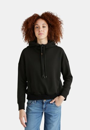 Felpa nera con cappuccio, tasca frontale, coulisse regolabili e orlo a coste. Abbinata a jeans azzurri con vestibilità comoda.