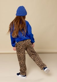 Blauwe gebreide trui, bruine panterprint broek, marineblauwe sneakers. Aanzienlijke lengte en ontspannen pasvorm, met een gestructureerde afwerking van de trui.