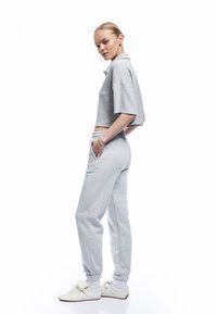 Lys grå cropped polo t-shirt med korte ærmer, parret med matchende joggerbukser med elastiske manchetter og sidelommer. Hvide sneakers.