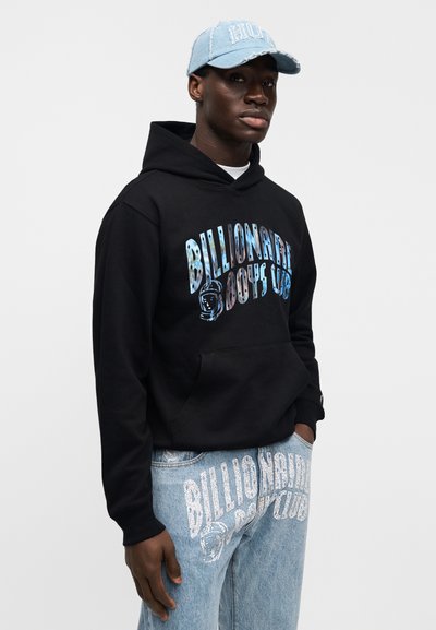 Μαύρο φούτερ με κουκούλα και πολύχρωμο γραφικό κείμενο "Billionaire Boys Club" και ανοιχτό μπλε τζιν τζιν με αντίστοιχο λογότυπο. Ανοιχτό μπλε καπέλο.