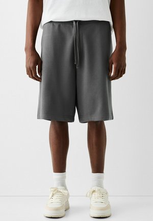 Szare bawełniane szorty z elastycznym pasem, detalem sznurkiem i bocznymi kieszeniami. Noszone z białymi trampkami i skarpetkami do wysokości kostek.