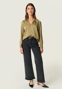 Olive green, long-sleeve blouse with a V-neck, paired with high-waisted, dark gray wide-leg jeans and black pointed-toe flats.
