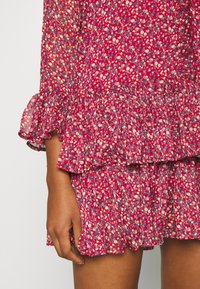 Red floral dress with ruffled sleeves and tiered skirt, featuring small white and blue flowers on a sheer fabric. Textured, lightweight material.