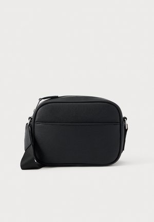 Petit sac bandoulière noir compact avec des bords arrondis, fermeture éclair sur le dessus et bandoulière en tissu réglable.