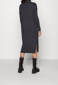 Długa, ciemnoszara sukienka golfowa z bocznymi rozcięciami, wykonana z miękkiego materiału dzianinowego. Połączona z czarnymi kozakiem do kolan z akcentami logo.