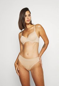 Sujeción beige sin costuras con copas moldeadas y tirantes ajustables, combinada con braguitas de bikini acanaladas a juego. Tela suave, herrajes mínimos.