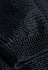 Ciemny dzianinowy materiał z detalami w postaci ściągacza, ukazujący teksturowane szwy i złożone warstwy w zbliżeniu.