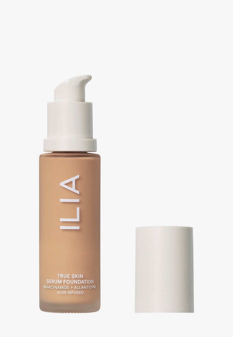 ILIA True Skin Serum Foundation lasitetussa lasipullossa, jossa on valkoinen pumppu ja kansi. Neste on lämmin beige väri, aloe-infusoitu.