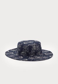 Marineblå stoffhatt med bred brem, prydet med hvite blomster mønstre. Designet har en rund krone og flate, jevne kanter.
