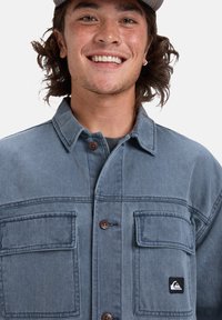 Jeansjacke in Hellblau mit zwei Brusttaschen und braunen Knöpfen. Mit einem Logo-Patch auf der linken Tasche. Strapazierfähiger Stoff, lockere Passform.