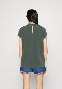 Top corto verde scuro a maniche corte con apertura a chiave sulla schiena, abbinato a pantaloni shorts di denim sfilacciati. Tessuto morbido, vestibilità rilassata e design minimalista.