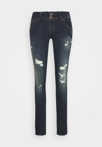 Jean skinny bleu foncé en denim, présentant des zones d'usure, une taille haute et une fermeture à double bouton à l'avant.