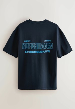 Tengerészkék pamut póló, élénk kék szöveggel, amelyen a "COPENHAGEN" felirat és koordináták találhatók, rövid ujjakkal és kerek nyakkivágással.