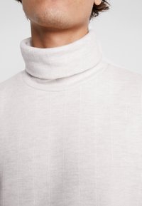 Suéter de cuello alto de canalé en gris claro, hecho de una tela suave, que presenta un cuello alto y una superficie texturizada para mayor interés visual.